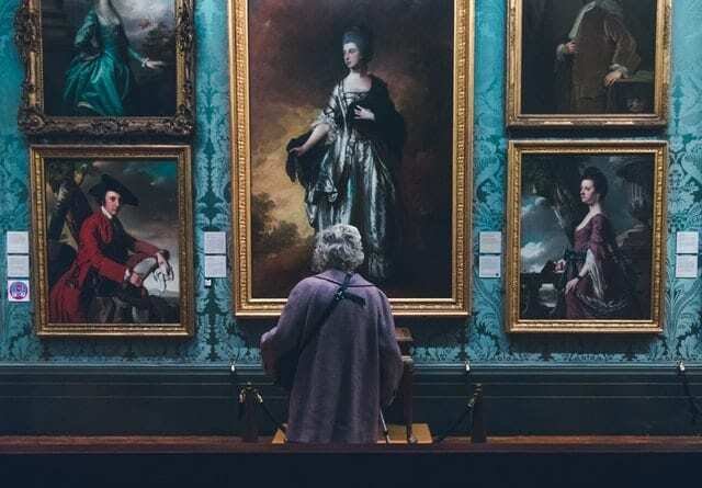 A woman looking at valuable paintings on a wall which shouldn't be kept in storage units.
